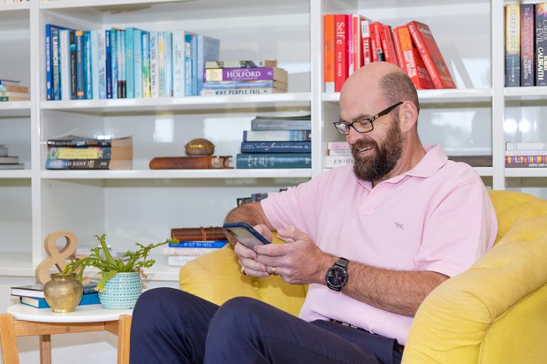 Randall sitting on couch looking at something funny on his phone 