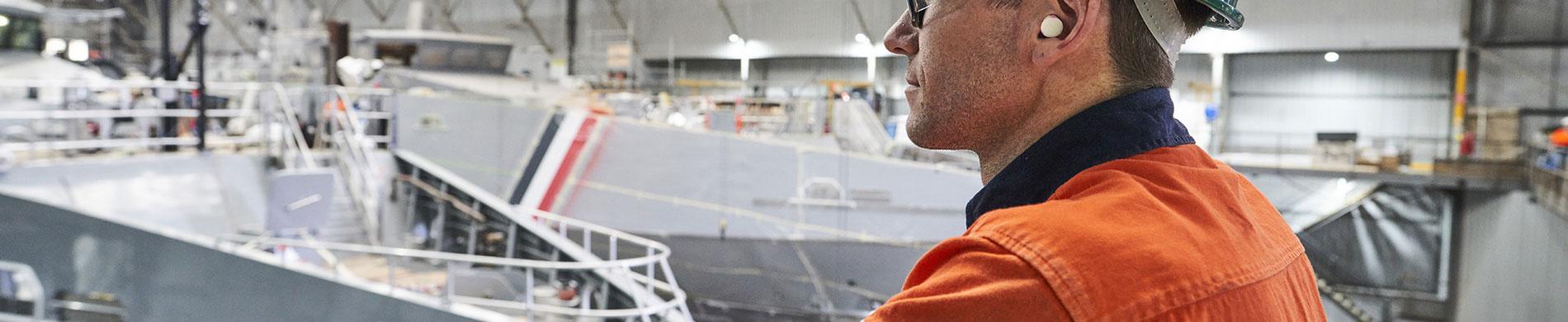 Man in high-vis with naval vessels under construction in the background