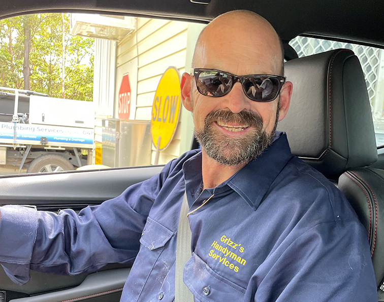 Man sitting in car wearing sunglasses and blue sandman shirt. 