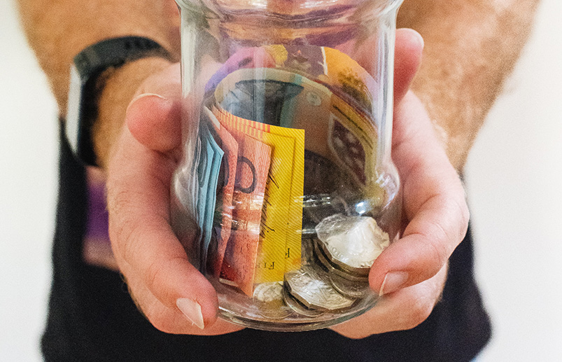 Man holding Australian currency notes and coins in a jar